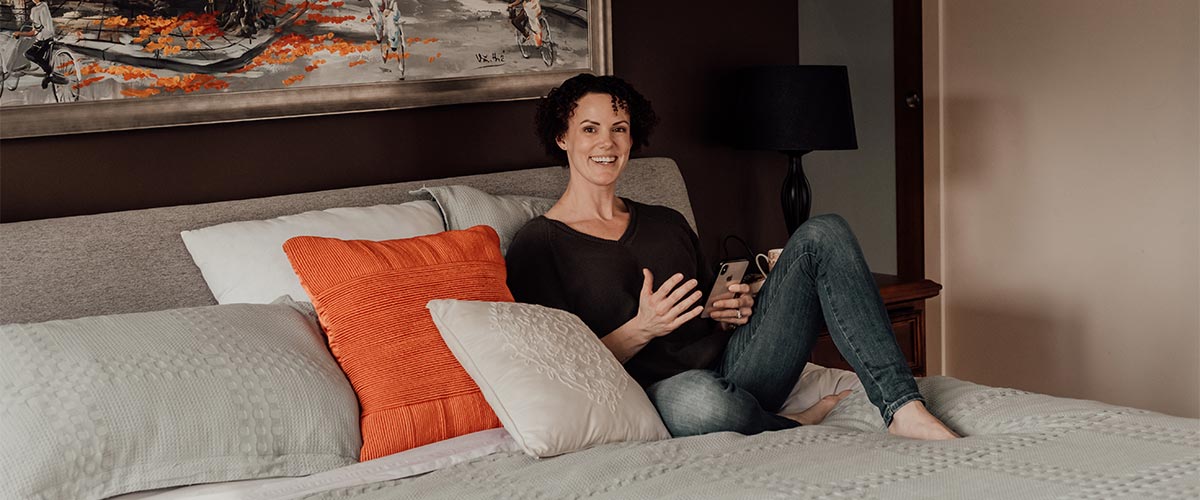 Rachel Clark sitting on a bed holding a phone, engaged in a conversation with her ongoing SEO clients.