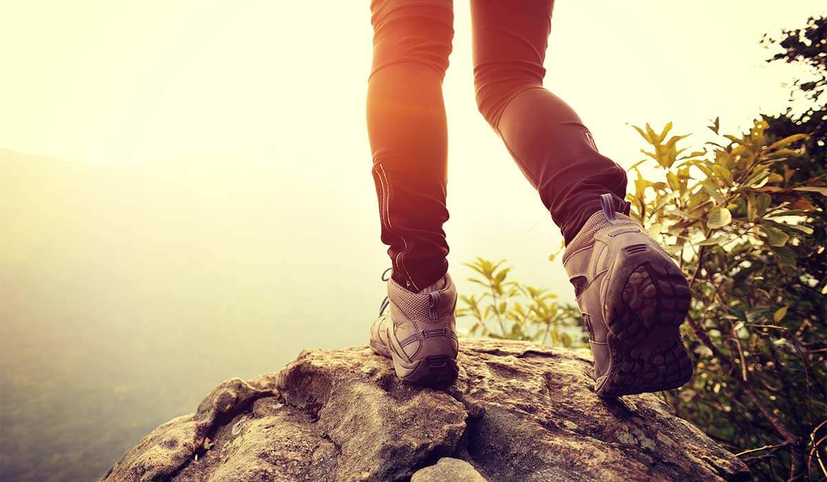 The feet of a business woman in hiking boots securely standing on top of a rock, showcasing her strength and balance.